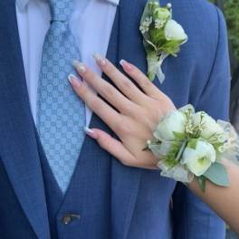 White floral wrist corsage and matching boutonniere worn with a blue suit