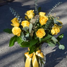 Arrangement of yellow roses with a yellow ribbon bow in a clear glass vase.