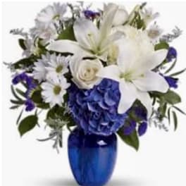 White lilies, roses, and daisies with blue hydrangea in a cobalt blue glass vase