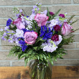 Mixed bouquet of pink roses, purple blooms, and lavender flowers in a clear glass vase