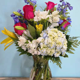 Mixed bouquet of roses, lilies, hydrangea, and blue flowers in a glass vase