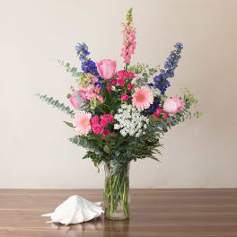 Tall pink, blue, and white mixed flower arrangement in a clear glass vase on a table