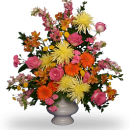 Tall mixed arrangement of pink roses, orange gerberas and yellow mums in a white pedestal vase