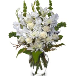 Tall arrangement of white lilies, roses, and mums with green accents in a clear glass vase