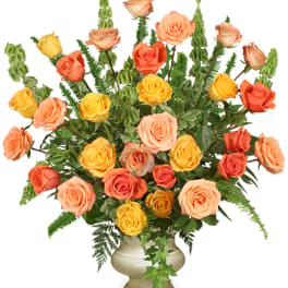 Tall arrangement of orange, peach, and yellow roses in a cream urn