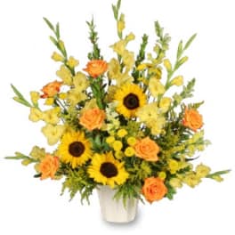 Tall arrangement of yellow sunflowers, orange roses, and yellow flowers in a white pot.