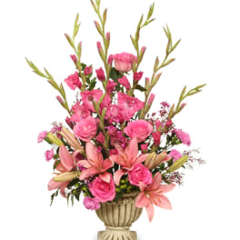 Tall pink arrangement of lilies, roses, and carnations in a cream pedestal urn vase