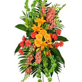 Tall standing spray with orange lilies and roses, pink snapdragons, and green bells of Ireland on an easel