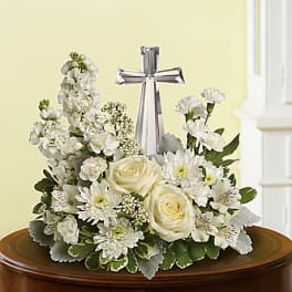 White floral arrangement with roses and a clear crystal cross on a low container