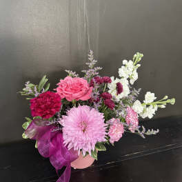 Low pink and white mixed flower arrangement in a pink vase with a purple ribbon bow
