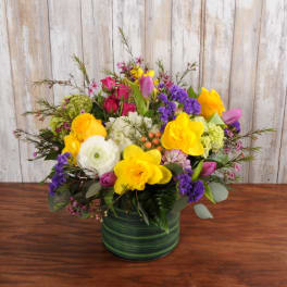 Low arrangement of yellow, purple, pink, and white flowers in a green striped vase