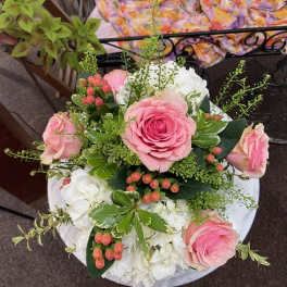 Round arrangement of pink roses with white hydrangeas and peach berries viewed from above.