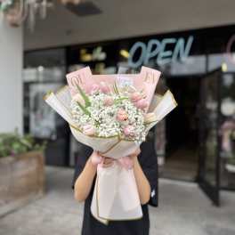 Hand-tied bouquet of light pink tulips and white filler flowers wrapped in pink and white paper with a ribbon.