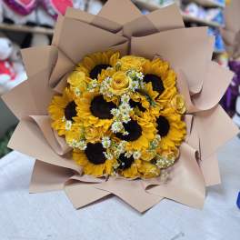 Bouquet of sunflowers, yellow roses, and small white daisies wrapped in tan paper