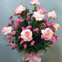 Tall arrangement of pink roses and pink filler flowers in a glass vase with a pink bow