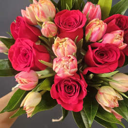 Hand-tied bouquet of hot pink roses and cream-pink tulips against a dark background