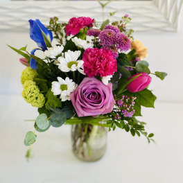 Colorful mixed bouquet with pink rose, carnations, daisies, tulip and iris in a clear glass jar vase