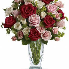 Tall glass vase of red, pink, and white roses and spray roses arranged in a rounded bouquet