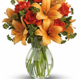 Orange lilies and red roses arranged in a clear glass vase