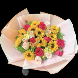 Round bouquet of yellow sunflowers with pink and ivory roses wrapped in soft pink paper