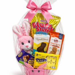 Easter gift basket with pink bunny plush, candies, and cookies wrapped in cellophane with a pink bow