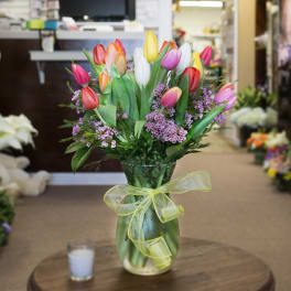 Mixed tulip bouquet with purple filler flowers in a glass vase tied with yellow ribbon