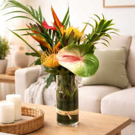 Tall tropical flower arrangement with protea and anthurium in a clear glass vase on a coffee table