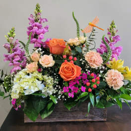 Rectangular wooden box filled with orange roses, pink carnations, purple snapdragons, and yellow blooms