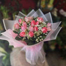 Hand-tied bouquet of pink tulips with small white filler flowers, wrapped in pink and white paper with a bow