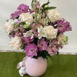Mixed pink and cream flower arrangement in a pink vase with a small white bunny figurine.