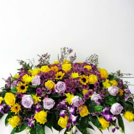 Elongated arrangement of yellow and lavender roses with purple orchids and daisies.
