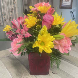 Bright bouquet of yellow daisies and pink roses in a red glass cube vase