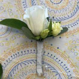 White rose boutonniere with small buds and greenery wrapped in white ribbon with pearl pins on patterned cloth
