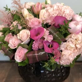 Low pink arrangement with roses, hydrangeas, tulips, and calla lilies in a black ceramic vase