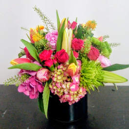 Colorful mixed bouquet with pink hydrangeas, red roses, tulips, and lilies in a black cylinder vase