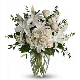 White lilies and roses with other white blooms arranged in a clear glass vase