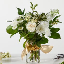 White and cream flowers in a clear glass vase with a gold ribbon bow