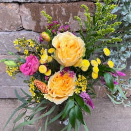 Mixed bouquet of yellow and pink blooms in a clear glass vase against a stone wall