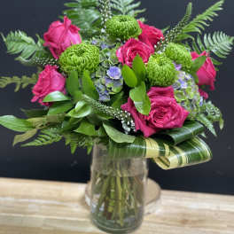 Vase arrangement of hot pink roses, green mums, and hydrangea with looped variegated leaves in a clear glass vase
