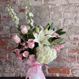 Pink roses and white lilies in a white vase with a pink ribbon