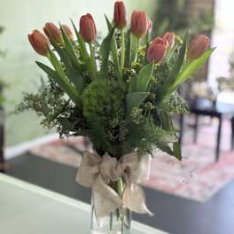 Pink tulips arranged in a clear glass vase with a burlap bow