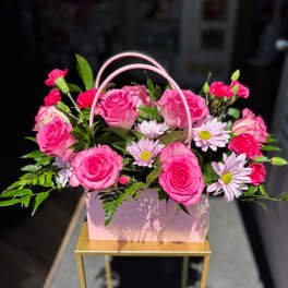 Pink roses and daisies arranged in a pink handled gift box