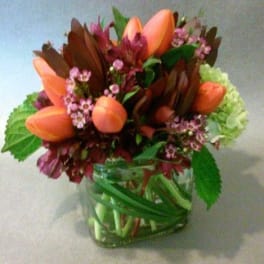 Orange tulips and pink flowers arranged in a glass vase
