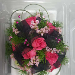 Pink roses with black ribbon and decorative greenery in a clear plastic box
