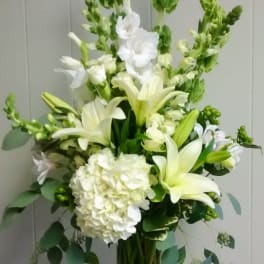 White lilies and hydrangea in a clear glass vase with tall green spikes