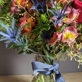 Mixed bouquet of pink and orange flowers in a glass vase with a blue ribbon