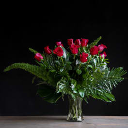 Red roses arranged in a clear glass vase with lush greenery