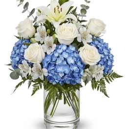 Blue hydrangeas and white roses in a clear glass vase