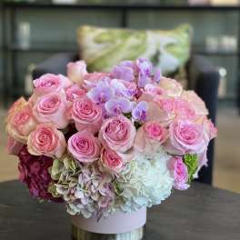 Pink roses and hydrangeas with purple orchids in a round box arrangement