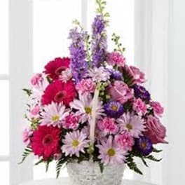 Basket arrangement of pink gerbera daisies, roses, and lavender blooms in a white woven basket
